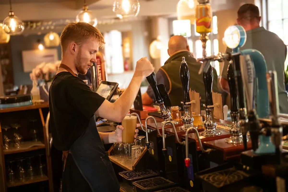Bartender pulling a pint under warm pendant lights